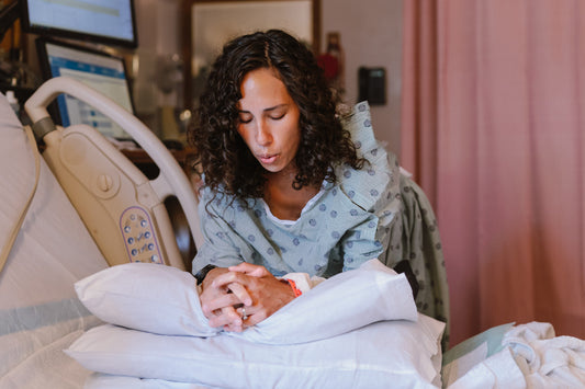 En gravid kvinna i en sjukhusklänning lutar sig över en kudde i en sjukhussäng, koncentrerad och fokuserad på att andas under förlossningsvärkar i en förlossningssal.
