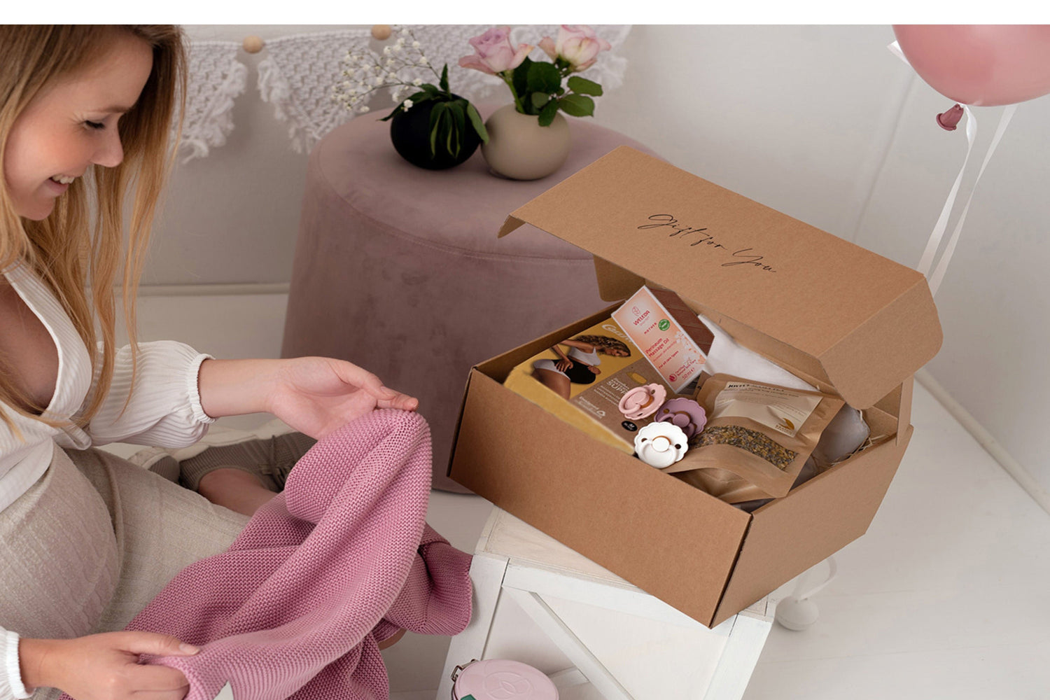 Gravid kvinna öppnar ByMini presentbox med handplockade produkter för nyblivna mammor och babyshowers.