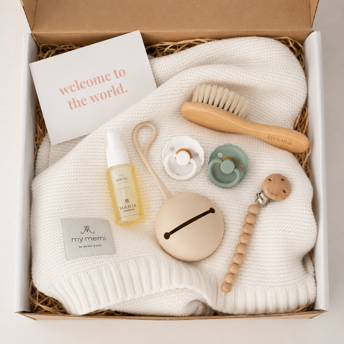 Vit babybox från BYMINI med stickad babyfilt, nappar, nappfodral, napphållare, babyolja och hårborste